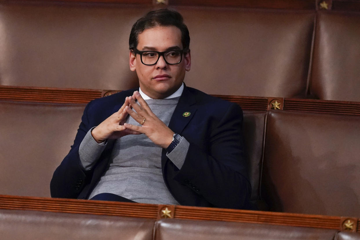 Rep. George Santos, fingertips touching, sits in his seat in the House looking watchful.