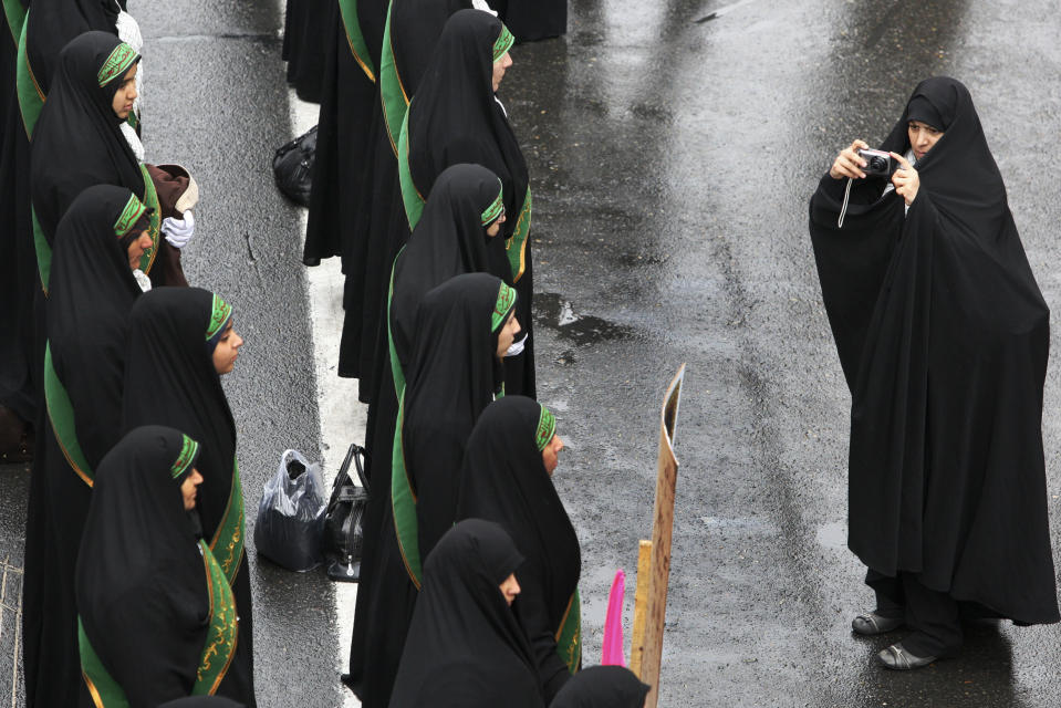 FILE - In this Nov. 25, 2011 file photo, female members of the Iranian paramilitary Basij force, affiliated with the Revolutionary Guard stand in formation as a woman photographs them in a rally in front of the former US Embassy in Tehran, Iran. On Monday, April 8, 2019, the Trump administration designated Iran’s Revolutionary Guard a “foreign terrorist organization” in an unprecedented move against a national armed force. Iran’s Revolutionary Guard Corps went from being a domestic security force with origins in the 1979 Islamic Revolution to a transnational fighting force.(AP Photo/Vahid Salemi, File)