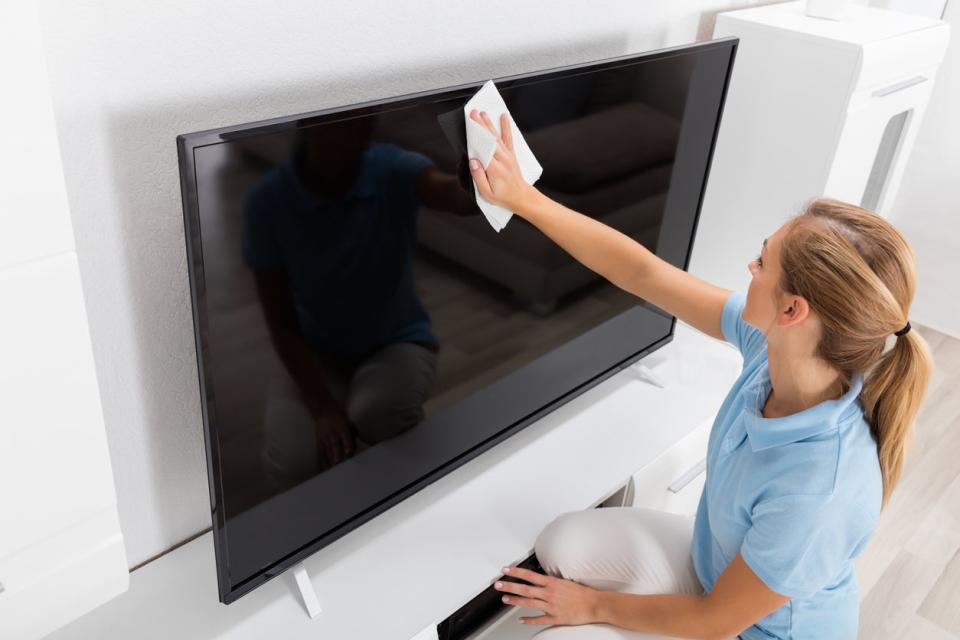 Young woman cleaning TV screen in a white living room