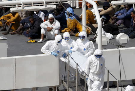 Armed Forces of Malta personnel in protective clothing carry the body of a dead immigrant off Italian coastguard ship Bruno Gregoretti as surviving migrants watch in Senglea, in Valletta's Grand Harbour, April 20, 2015. REUTERS/Darrin Zammit Lupi