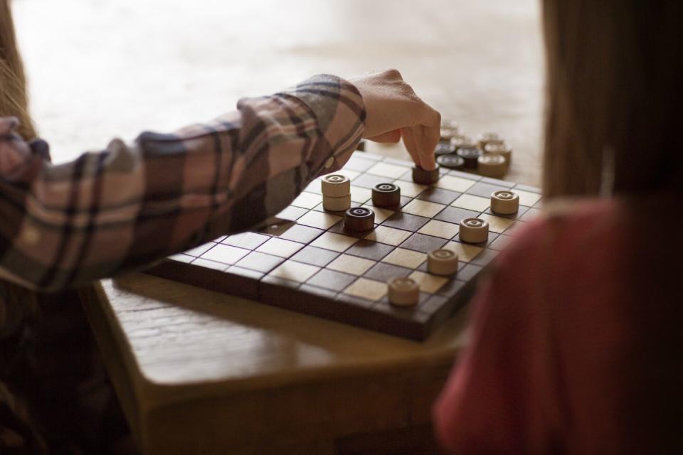 two sisters playing draughts board game on a dining table
