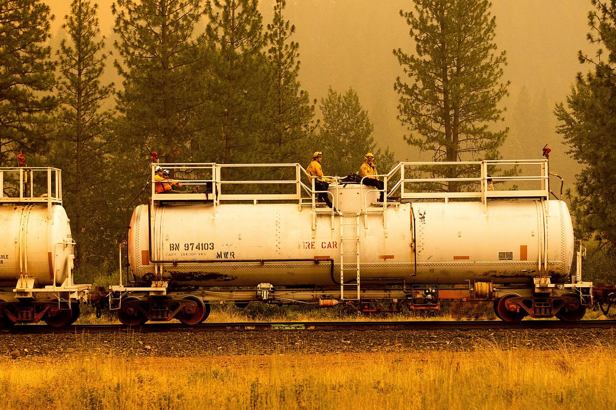 Firefighters ride atop a fire train while battling the Dixie Fire in Plumas County, Calif. on Saturday, July 24, 2021. The train is capable of spraying retardant to coat tracks and surrounding land.