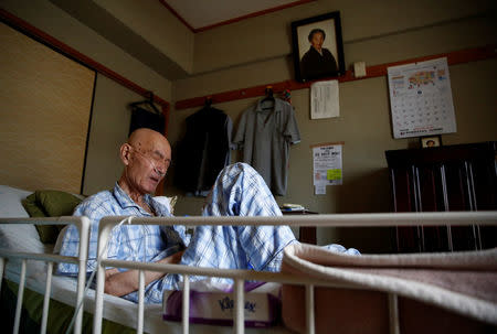 Yasuhiro Sato, 75, and has terminal lung cancer, grimaces with pain in his bed in Tokyo, Japan, July 19, 2017. A portrait of his grandmother hangs on the wall. REUTERS/Kim Kyung-Hoon