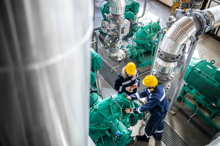 Two people wearing personal protective equipment and working in an industrial setting. 