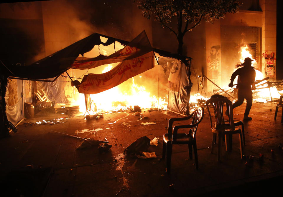 An anti-government protester tries to extinguishes his tent which set on fire by civilian men believed to be the private unit of the parliament guards, during ongoing protests against the political elites in Beirut, Lebanon, Saturday, Jan. 18, 2020. Riot police fired tear gas and sprayed water cannon near parliament in Lebanon's capital Saturday to disperse thousands of protesters after riots broke out during a march against the ruling elite amid a severe economic crisis. (AP Photo/Hussein Malla)