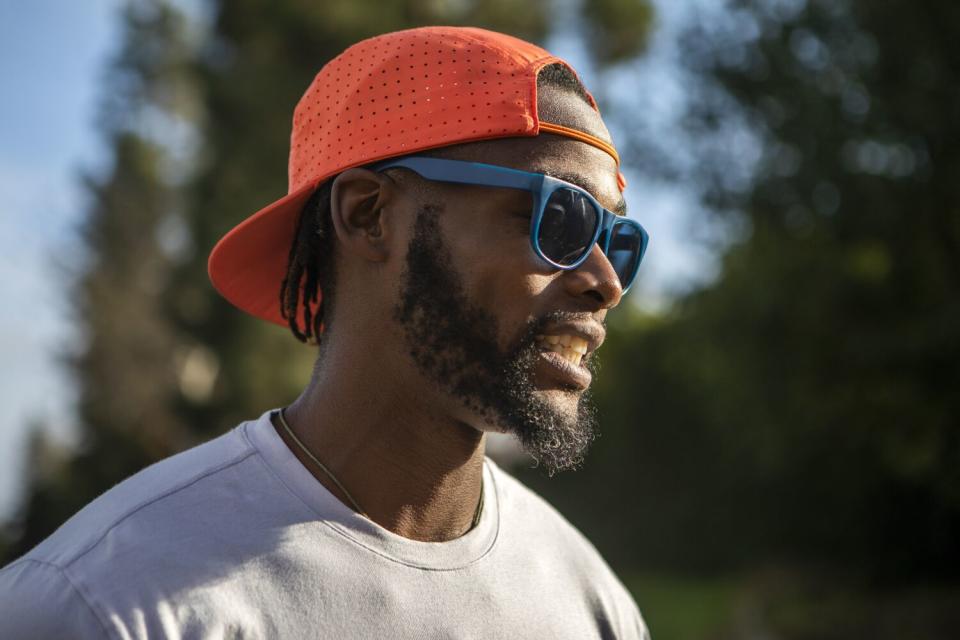 Oliver James, a young Black man, wears blue sunglasses and a neon-orange hat.