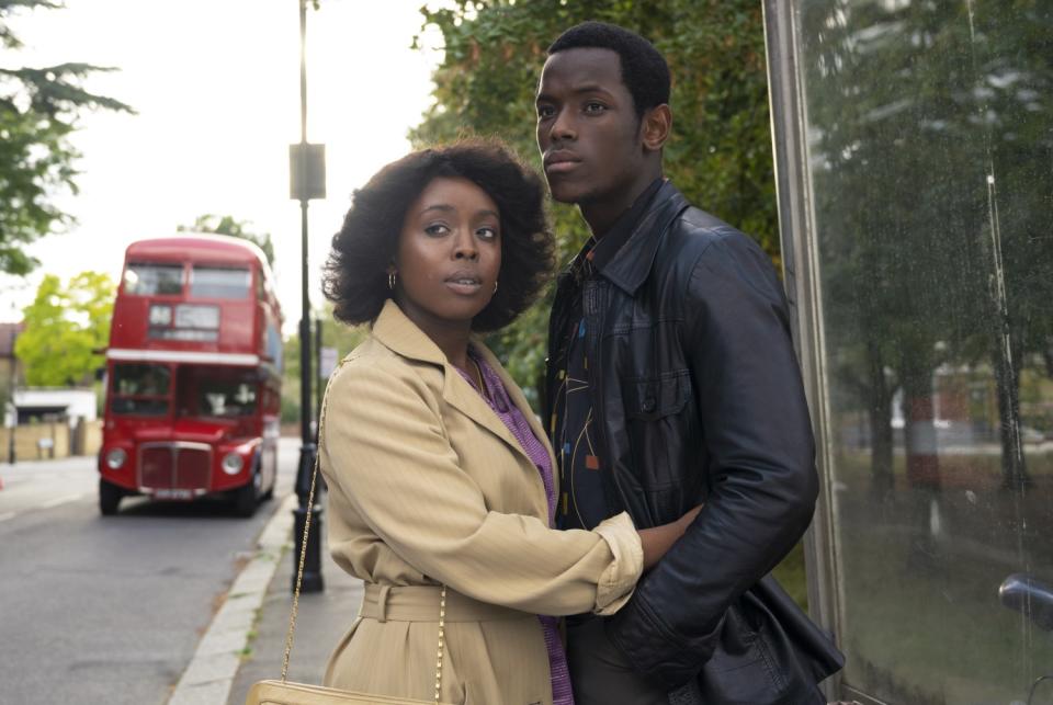 A couple embracing on the sidewalk with a red London bus behind them