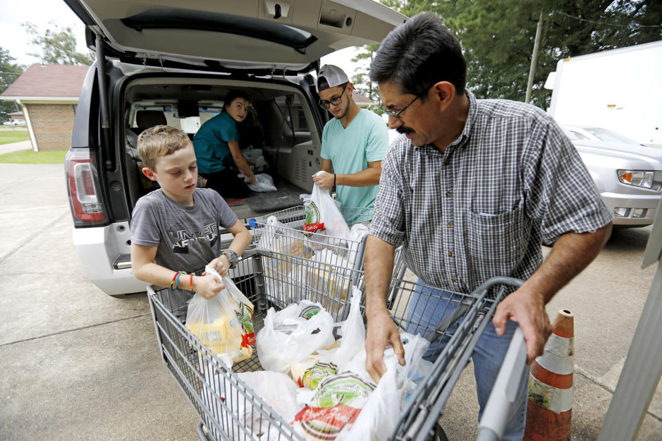 In this Thursday, Aug. 8, 2019 photo, Pastor Hugo Villegas, right, and his son Pablo Villegas, second from right, assist Cade Vowell, left, and his sister Addison Vowell, second from left, unload donated items for the pantry at the Carlisle Crisis Center in Forest, Miss. The center, a ministry of Scott County Baptist Association, says they will need more food items to help out the families affected by the fallout of Wednesday's raid by U.S. immigration officials at poultry plants Koch Foods and PH Foods in neighboring Morton. The raids were part of a large-scale operation targeting owners as well as undocumented employees. (AP Photo/Rogelio V. Solis)