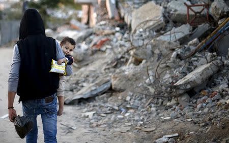 A Palestinian holds his son as they walk past houses that witnesses said were destroyed during a 50-day war last summer, in the east of Gaza City May 4, 2015. REUTERS/Mohammed Salem