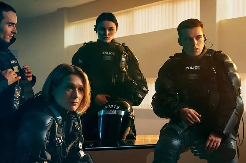 The four characters dressed up in police gear, sat in a police station