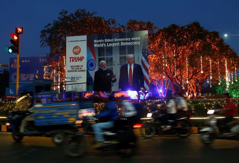 People ride their motorbikes past a hoarding with the images of India's Prime Minister Narendra Modi and U.S. President Donald Trump, in Ahmedabad