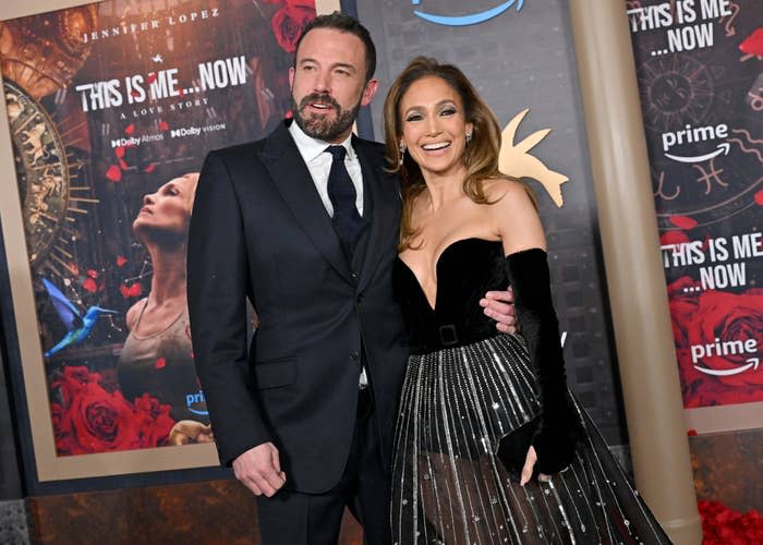 Ben Affleck and Jennifer Lopez pose together at a red carpet event. Ben Affleck is in a suit, and Jennifer Lopez is in an elegant dress with a corset-style bodice and a pleated skirt