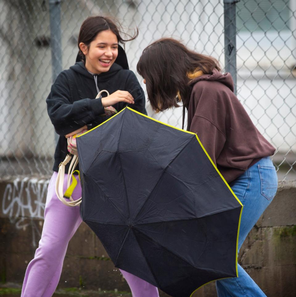 Sisters Megan Corrales, 15, left, and Bailey Corrales, 16, laugh as they struggle with their umbrella in the wind and the rain during an outing in Eugene Tuesday as a storm moves through the Pacific Northwest.