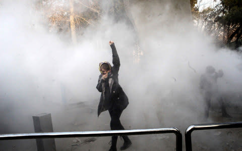 An Iranian woman raises her fist amid the smoke of tear gas at the University of Tehran during a protest driven by anger over economic problems, in the capital Tehran on December 30, 2017 - Credit: AFP PHOTO / STRSTR/AFP/Getty Images