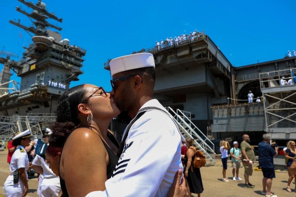 A US Navy sailor embraces his wife with USS Dwight D. Eisenhower in the background