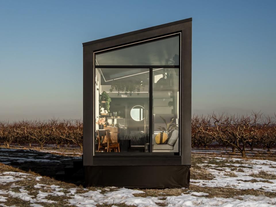 a black tiny home with a large glass wall on a snowy field at sunset