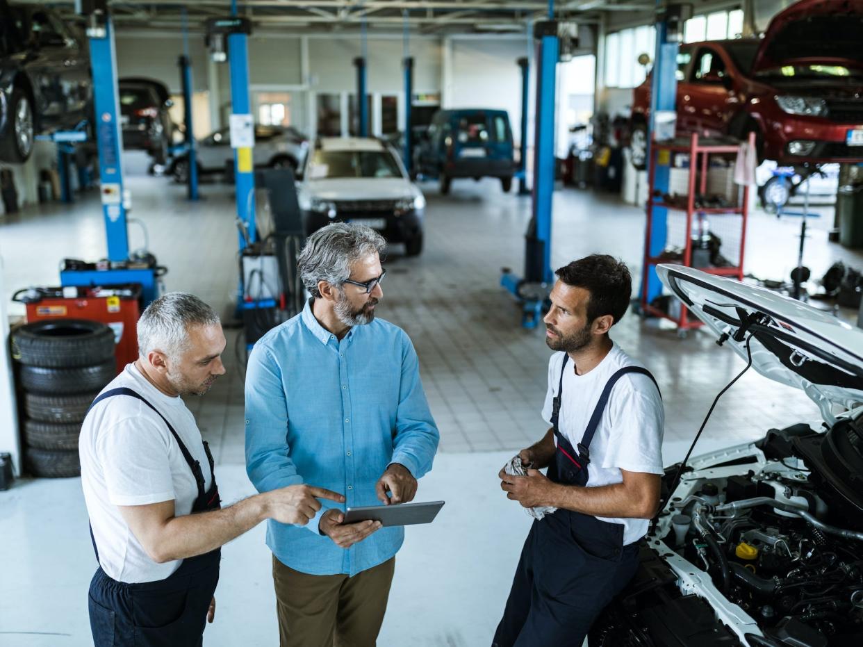 Manager using digital tablet while talking to mechanics in auto repair shop