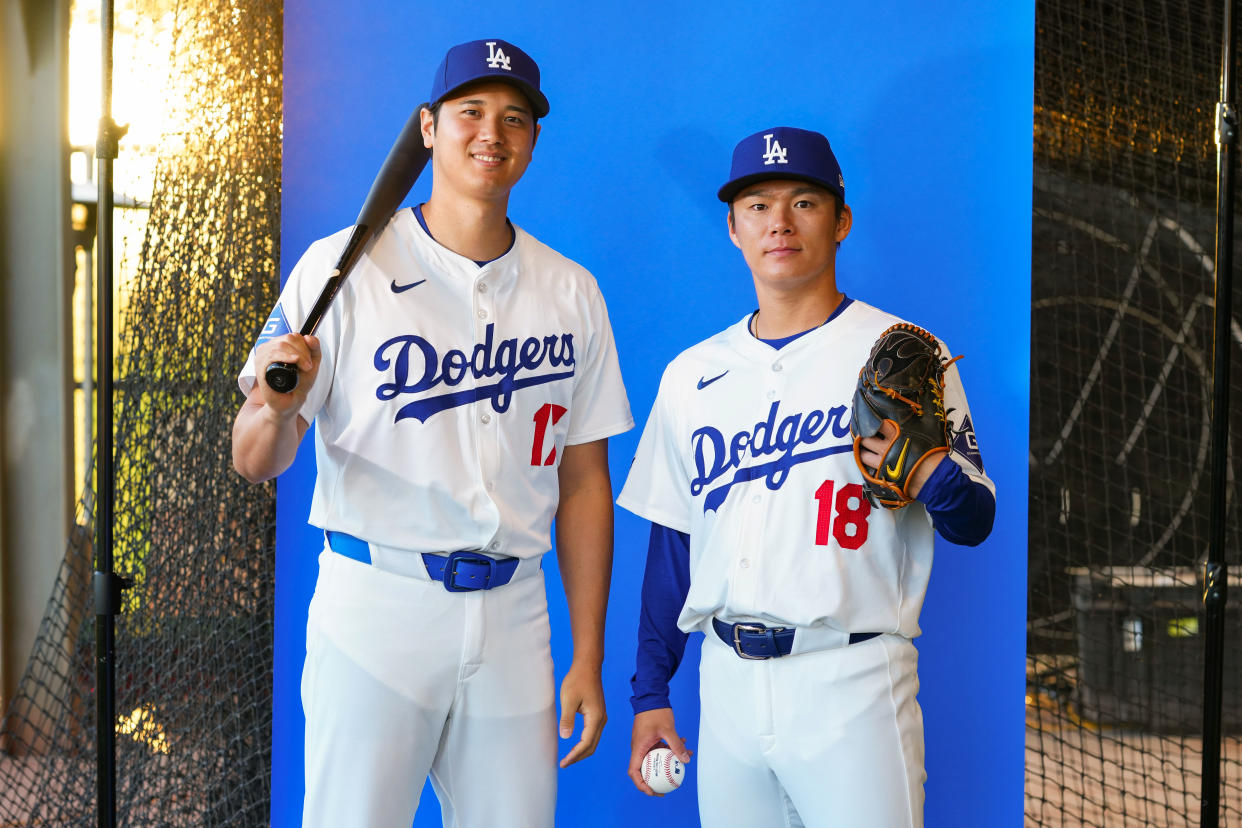 Shohei Ohtani (17) y Yoshinobu Yamamoto (18) muestran los nuevos uniformes de Los Angeles Dodgers, en el campamento de primavera de Grandes Ligas. (Foto: Mary DeCicco/MLB Photos via Getty Images)