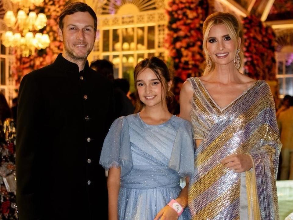 Three people dressed in traditional Indian clothing smile at the camera