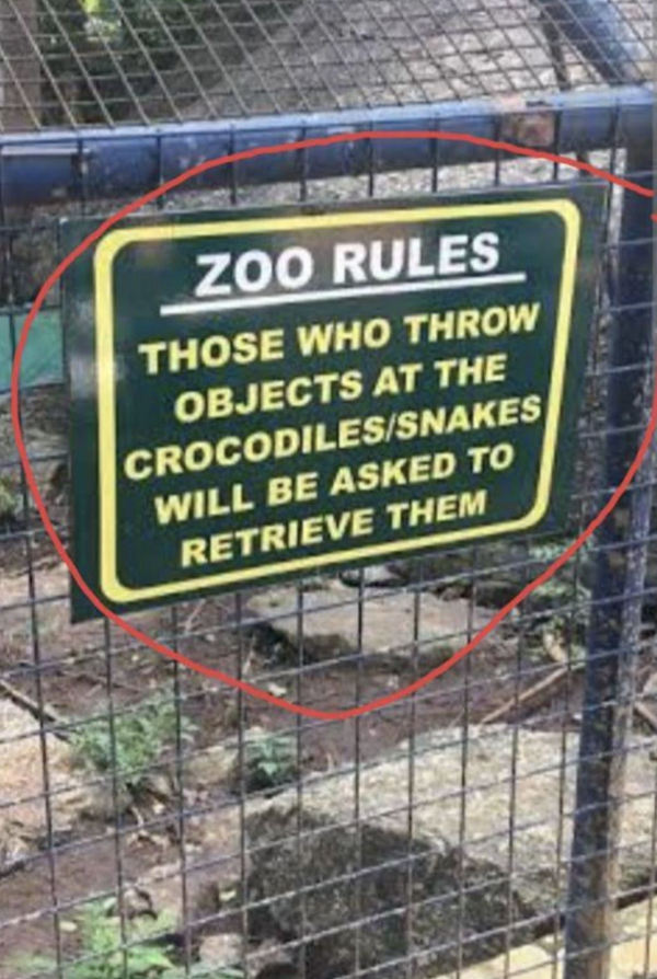 Sign reads "ZOO RULES THOSE WHO THROW OBJECTS AT THE CROCODILES/SNAKES WILL BE ASKED TO RETRIEVE THEM" with a red circle around it