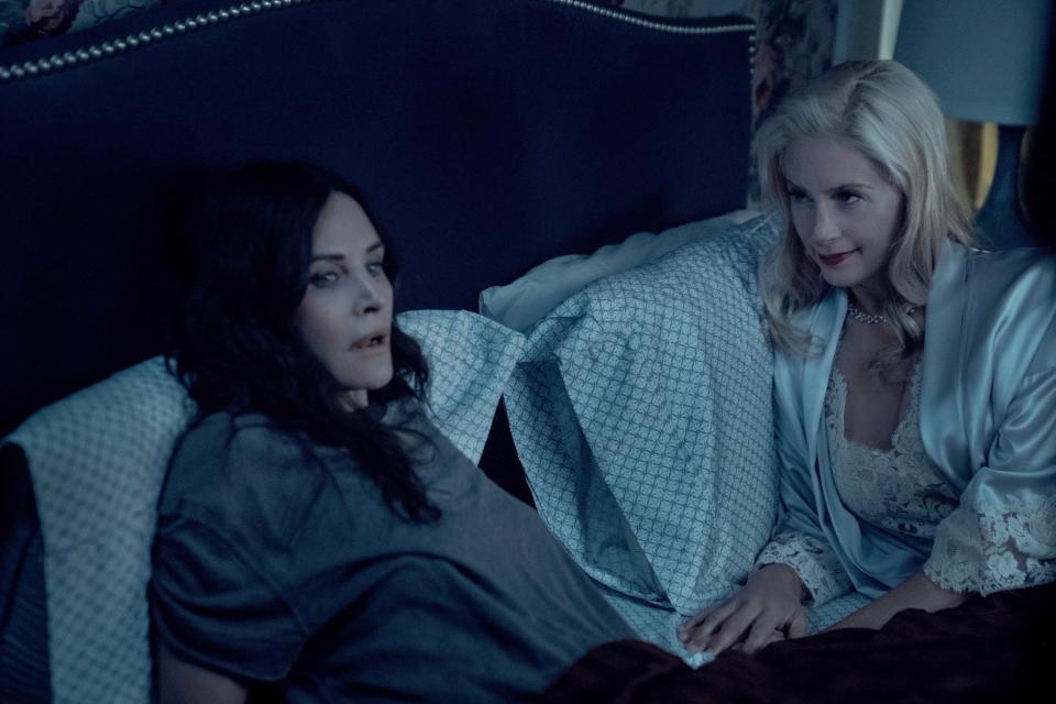 Courteney Cox is lying in bed while Mira Sorvino lies next to her and looks at her