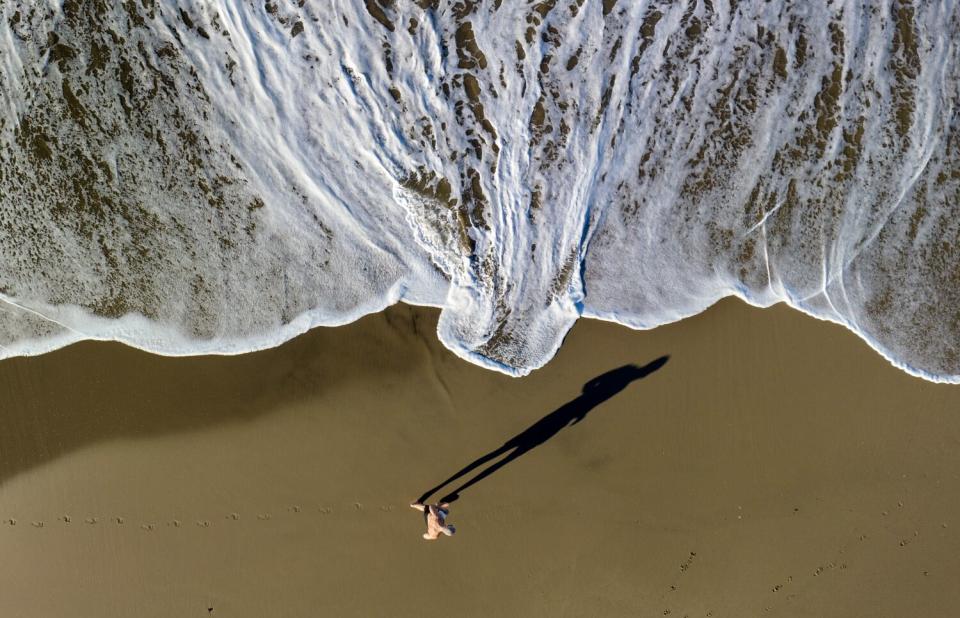 A man casts a long shadow as he jogs along the surf line.