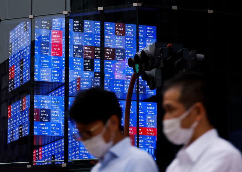 People pass by an electronic screen showing Japan's Nikkei share price index inside a conference hall in Tokyo