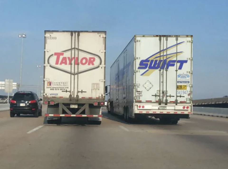 Two trucks labeled "Taylor" and "Swift" are side by side on a highway, creating an amusing visual pun referencing the singer Taylor Swift