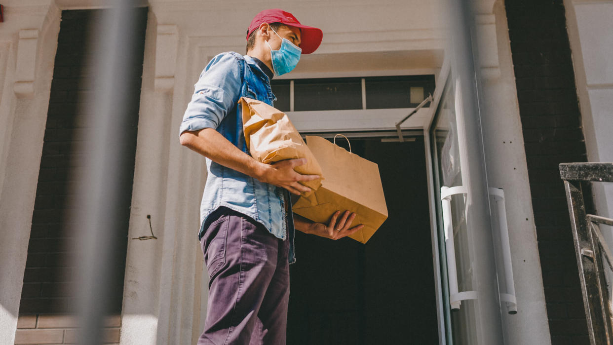 Delivery man holding paper bag with food on white entrance of house background , food delivery man in protective mask.