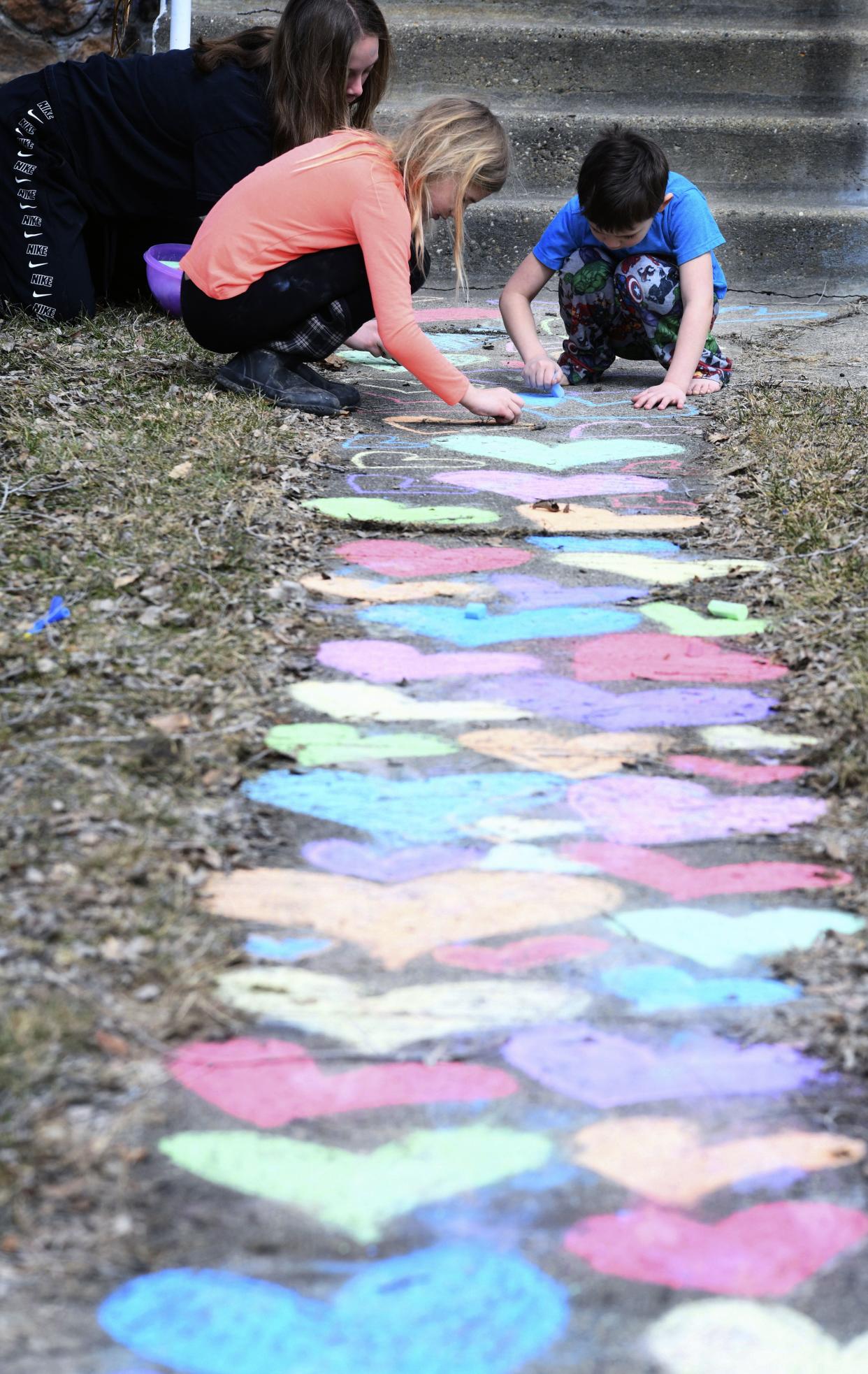 Tanna Crouse, 13, left, Greta Sticha, 8, middle, and her brother Elam, 5, use chalk to color a path of hearts leading to a home's front steps on Tuesday, March 24, 2020 in Bismarck. The hearts are a symbolic gesture of solidarity and a way for people to stay connected while staying at home due to the coronavirus pandemic forcing school closures and social distancing in North Dakota. (Mike McCleary/The Bismarck Tribune via AP)