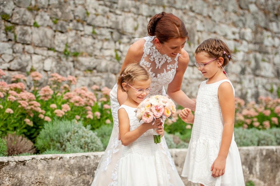 A bride smiles and speaks to two flower girls