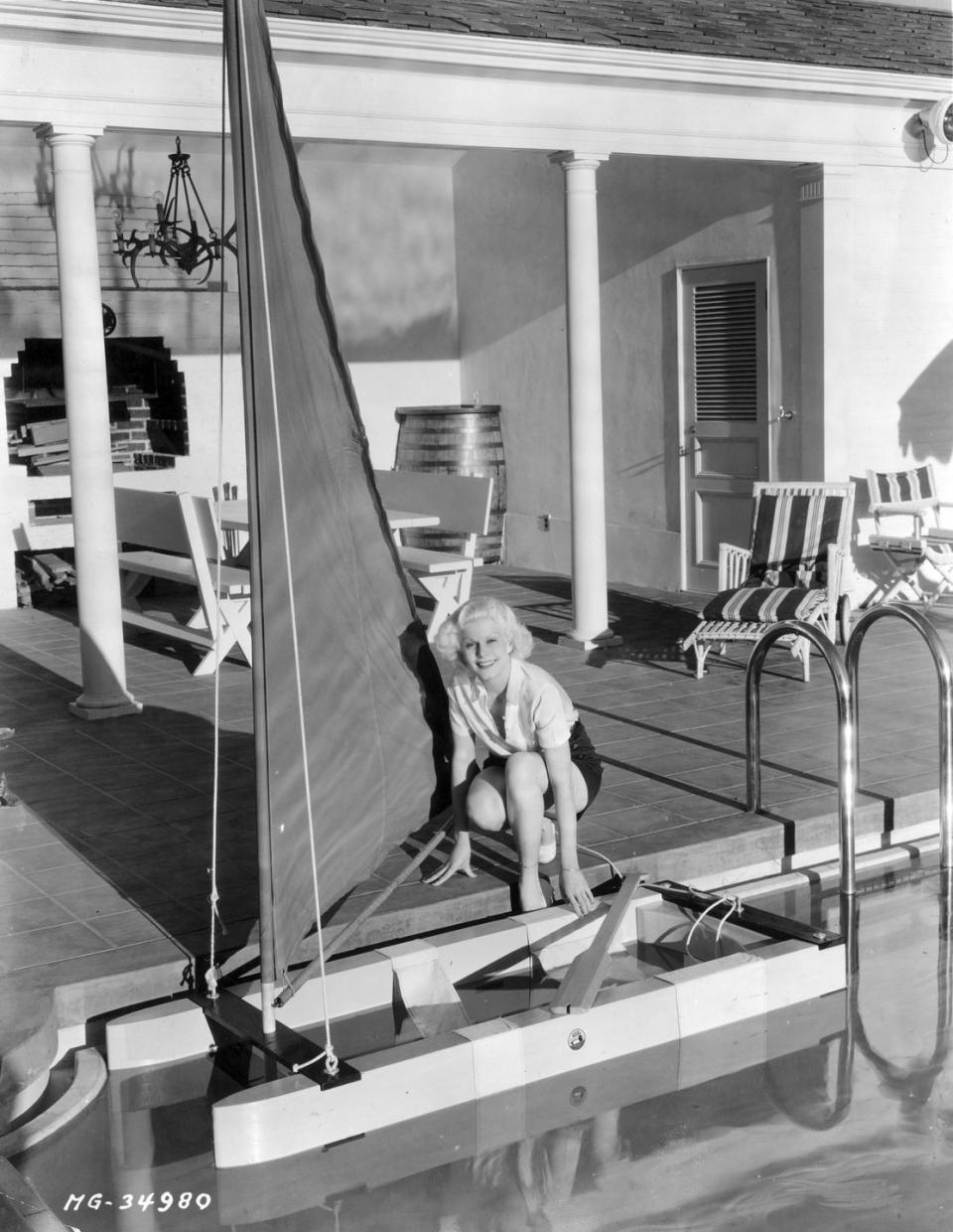 <p>The original blonde bombshell poses poolside next to a small sailboat, circa 1920s.</p>