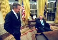 President George W. Bush talks to his father, former President Bush as he sits at his desk in the Oval Office for the first time on Inaugural Day, Jan. 20, 2001. (AP Photo/Eric Draper, White House)