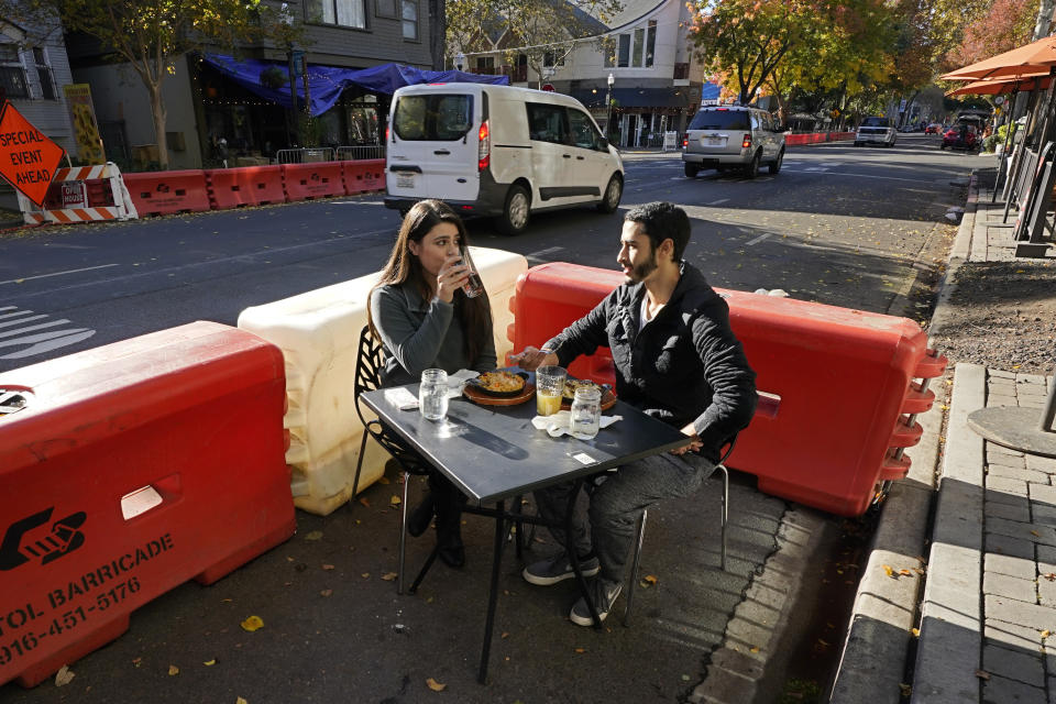 Ranim Abaad and Joey Bettencourt, right, have lunch at the RIND in Sacramento, Calif., Friday, Nov. 20, 2020. The city has put up protective barricades in street parking areas to allow restaurants to space out the dining areas to follow social distancing guidelines due to the COVID-19 pandemic. California on Saturday will join other states in trying a partial overnight curfew to stem a surge in coronavirus cases. The curfew from 10 p.m. to 5 a.m. will force some eateries to shorten their hours of operations, although restaurants can stay open for takeout and delivery after 10 p.m. (AP Photo/Rich Pedroncelli)