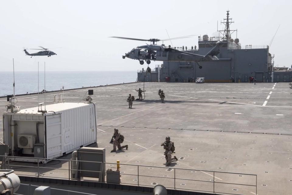 marines stand on the flight deck of an ESB while a helicopter hovers above