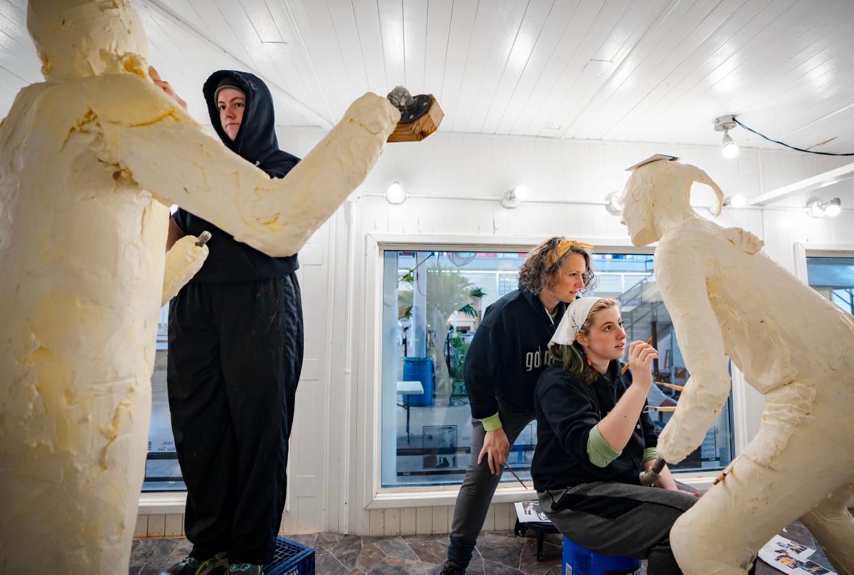 Grace Pratt, left, works on a sculpture of quarterback Kurt Warner while Hannah and her mother, Sarah Pratt, look over the lettering on Caitlin Clark's jersey in the butter cooler in the Iowa State Fair's agriculture building.