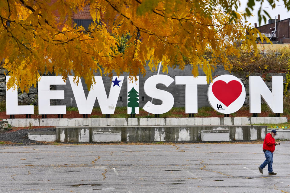 A man walks past a make-shift memorial at the base of the Lewiston sign at Veteran's Memorial Park, Sunday, Oct. 29, 2023, in Lewiston, Maine. The community is working to heal following shooting deaths of 18 people at a bowling alley and a bar in Lewiston on Wednesday, Oct. 25. (AP Photo/Matt York)