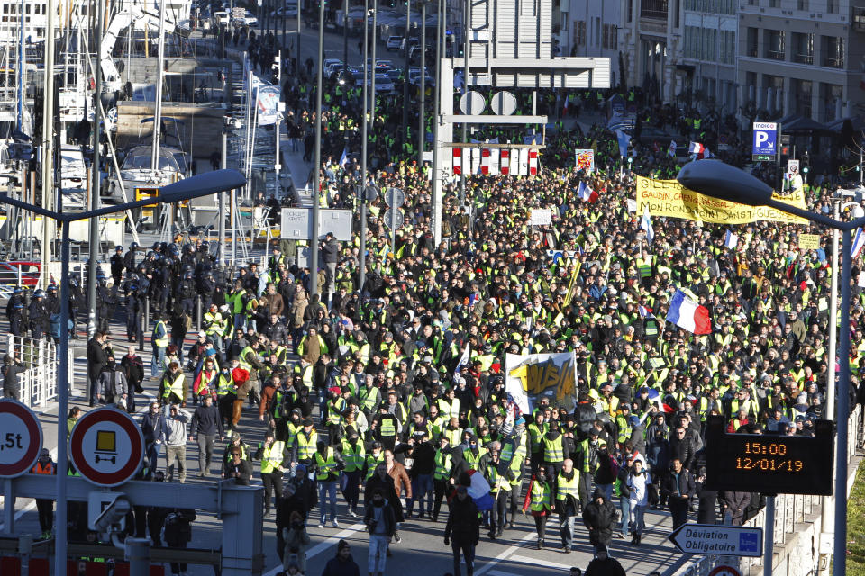 Yellow vest protesters pass through the old harbor as they demonstrate in Marseille, southern France, Saturday, Jan. 12, 2019. Paris brought in armored vehicles and the central French city of Bourges shuttered shops to brace for new yellow vest protests. The movement is seeking new arenas and new momentum for its weekly demonstrations. Authorities deployed 80,000 security forces nationwide for a ninth straight weekend of anti-government protests. (AP Photo/Claude Paris)