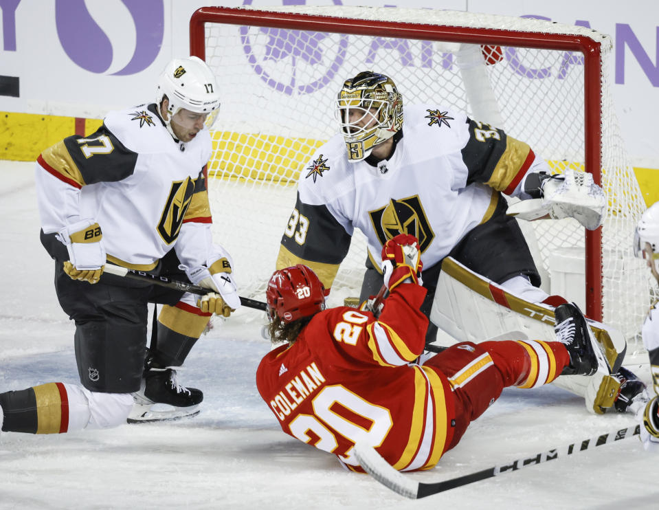 Vegas Golden Knights defenseman Ben Hutton, left, takes out Calgary Flames forward Blake Coleman (20) in front of Golden Knights goalie Adin Hill (33) during second-period NHL hockey game action in Calgary, Alberta, Monday, Nov. 27, 2023. (Jeff McIntosh/The Canadian Press via AP)