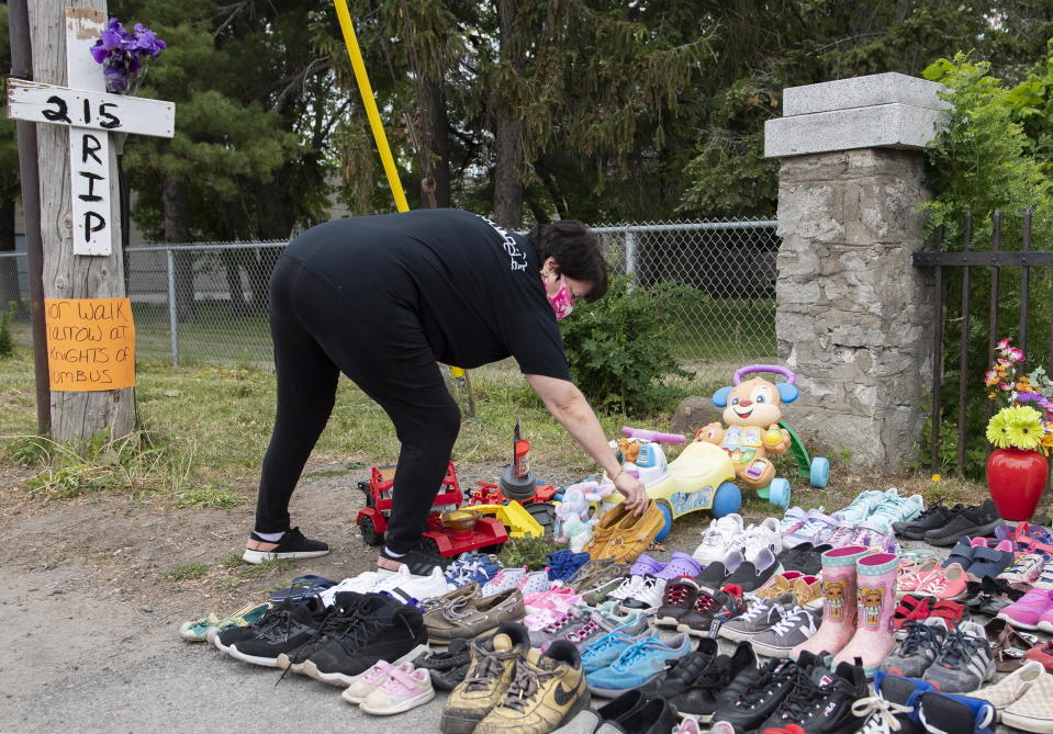 A woman places children's moccasins as a tribute to all the victims of the residential school system outside St. Francis Xavier Church in Kahnawake, Quebec, Sunday, May 30, 2021. (Graham Hughes/The Canadian Press via AP)