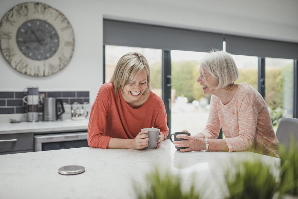 Senior woman is enjoying a catch up with her daughter. They are sitting in the kitchen drinking cups of tea. 