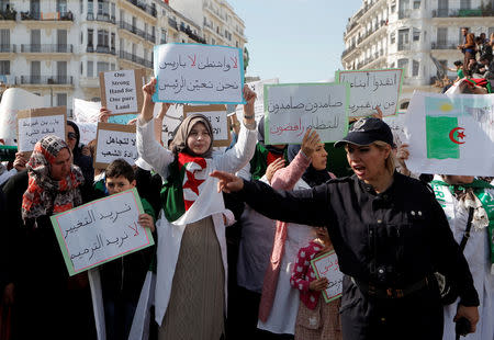 A police officer directs traffic while demonstrators carry signs as teachers and students take part in a protest demanding immediate political change in Algiers, Algeria March 13, 2019. The signs read: "We want change, we don't want restoration" and "No Washington, No Paris, we appoint the President" and "Resistance, resistance, we reject the system". REUTERS/Zohra Bensemra