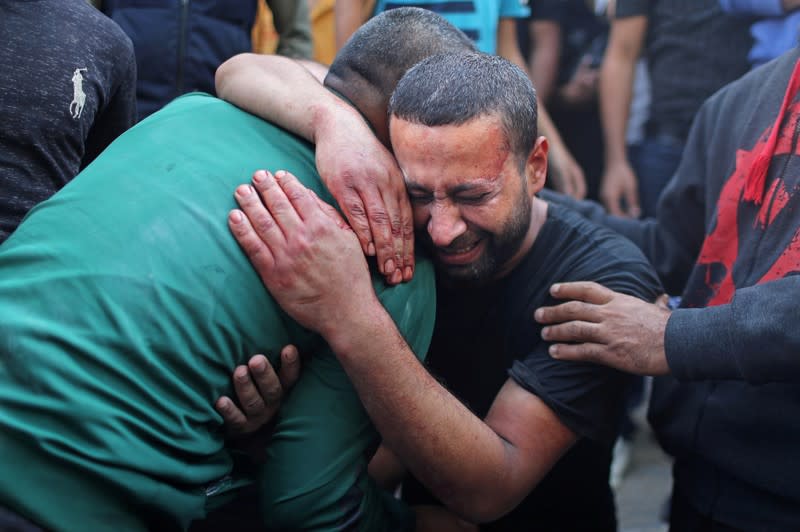 Palestinian man, stained with the blood of his relative, is comforted as he reacts at Shifa hospital in Gaza City