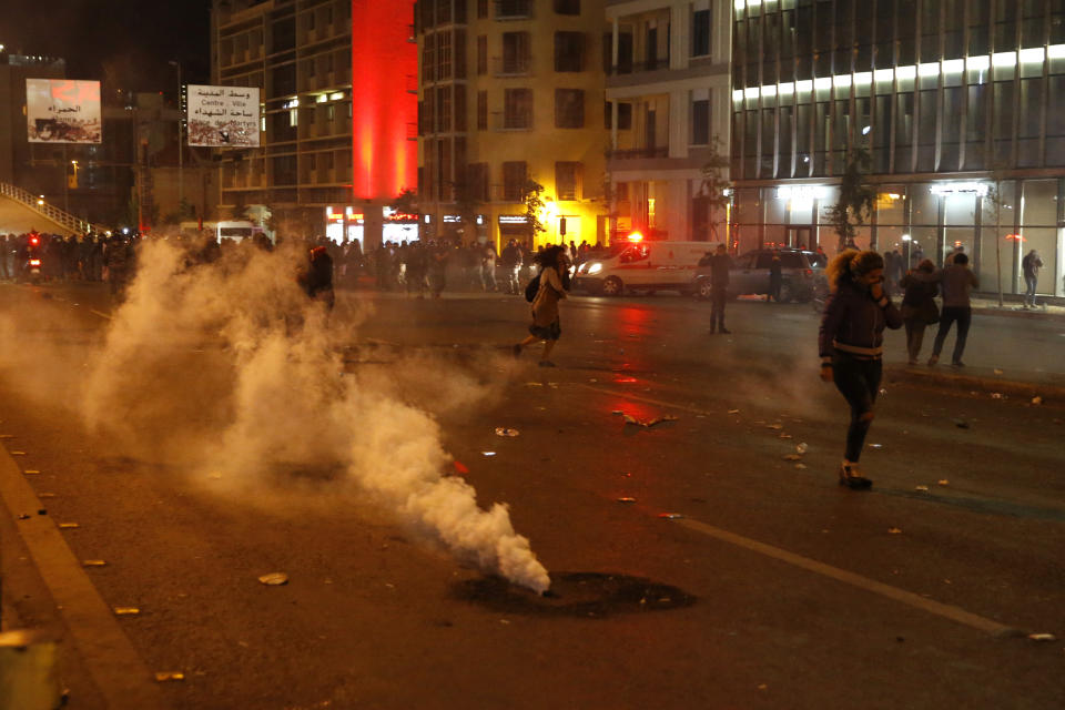 Protesters cover their faces from the tear gas that fired by the riot police during an anti-government protest in Beirut, Lebanon, Wednesday, Dec. 4, 2019. Protesters have been holding demonstrations since Oct. 17 demanding an end to corruption and mismanagement by the political elite that has ruled the country for three decades. (AP Photo/Bilal Hussein)