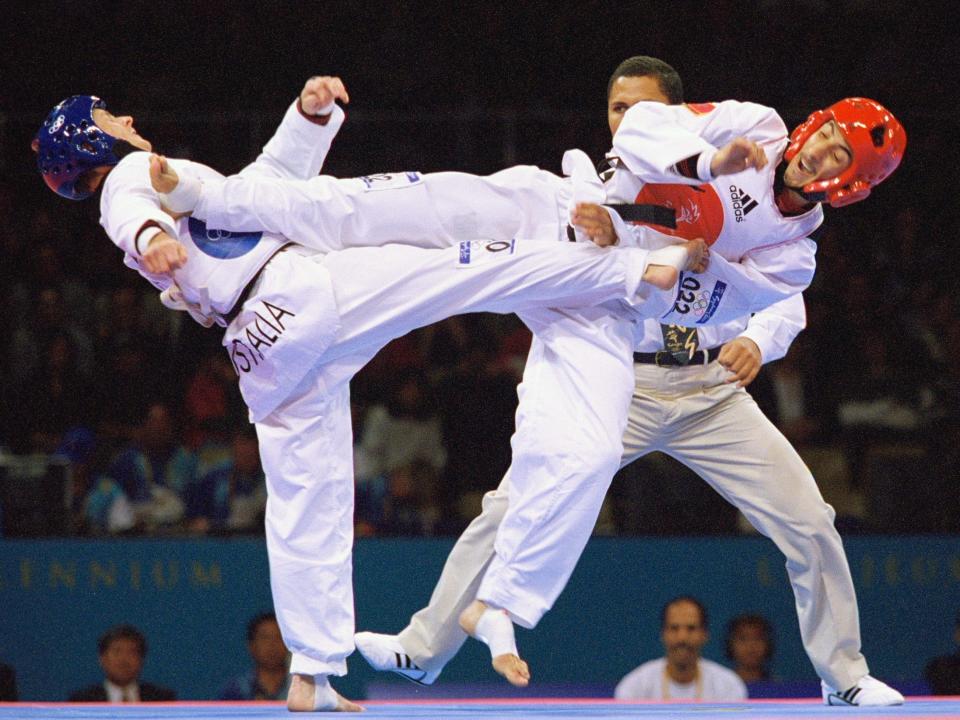 Two olympic athletes karate-kick each other at the same time with a crowd watching in the background.