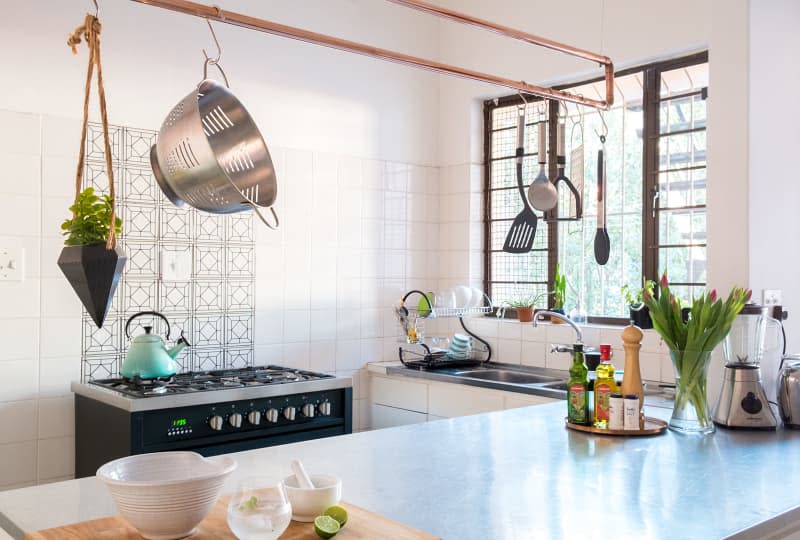 A copper pipe hung from the ceiling that holds kitchen utensils over a kitchen island