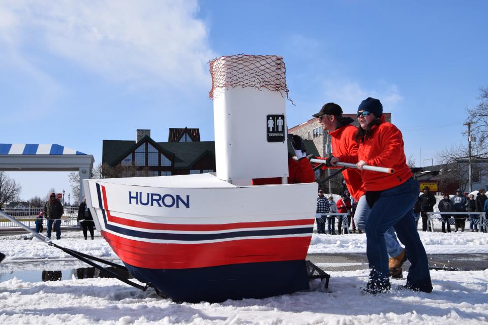 The rider in the "Mighty Huron" outhouse waves at the crowd from their make-shift restroom. Each team had five participants, two in front of the float, two behind, and one rider.