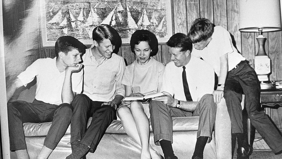 chip, jack, rosalynn, jimmy, and jeff carter sit on and around a couch and look at a book that rosalynn holds