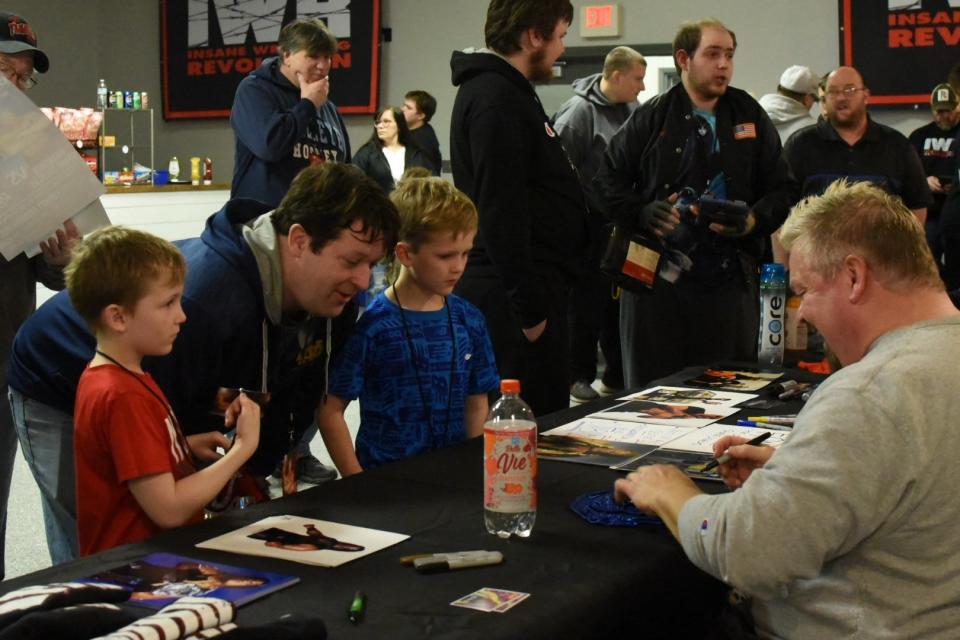 Elijah Gardner, 8, and Lincoln Gardner, 9, wait with their dad Zach Gilks, all of Fremont, as they get their wrestling masks signed by pro wrestler Franchise Shane Douglas at an Insane Wrestling Revolution event at the Ottawa County Fairgrounds in Oak Harbor on Wednesday.