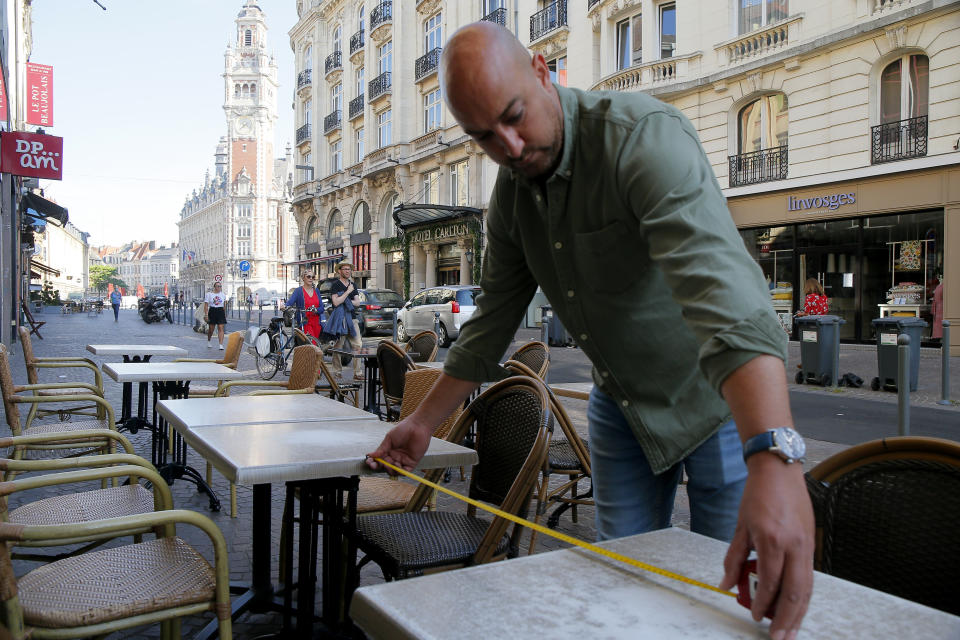 Un hombre mide la distancia entre las meses para respetar las normas de distanciamiento social en un café en Lille, en el norte de Francia, el martes 2 de junio del 2020. (AP Foto/Michel Spingler)